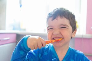 A cheerful young boy in pajamas brushing his teeth in a brightly lit bathroom.